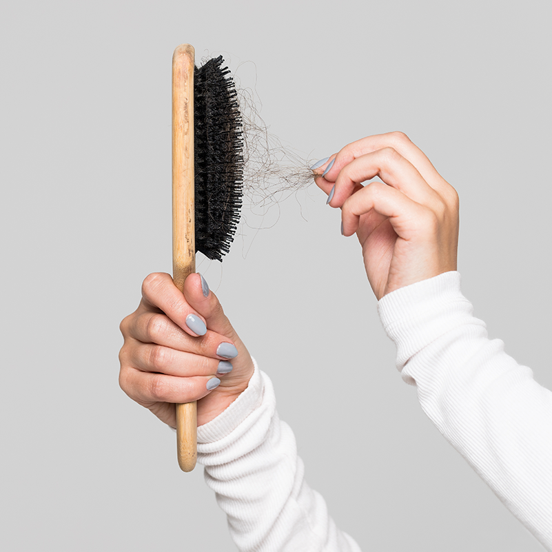 Frau zieht Haare aus Bürste, stellvertretend für Haarausfall